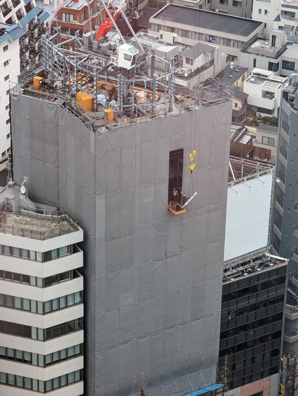 Edificio en construcción con grúa y trabajadores recibiendo material en altura.