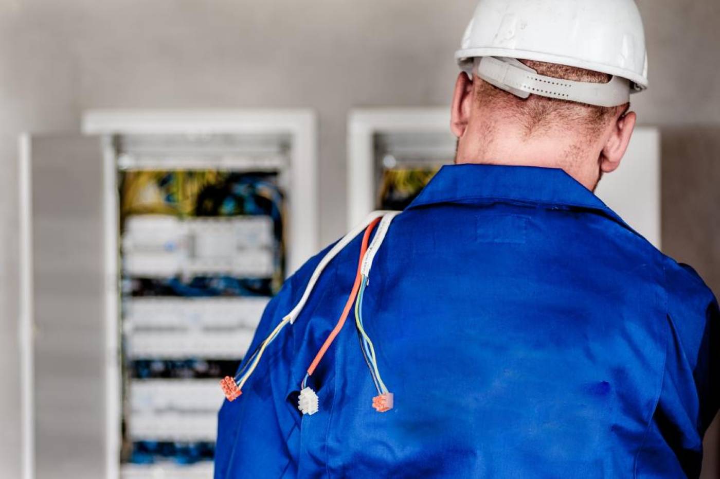 Técnico con casco y overol trabajando frente a tableros eléctricos.