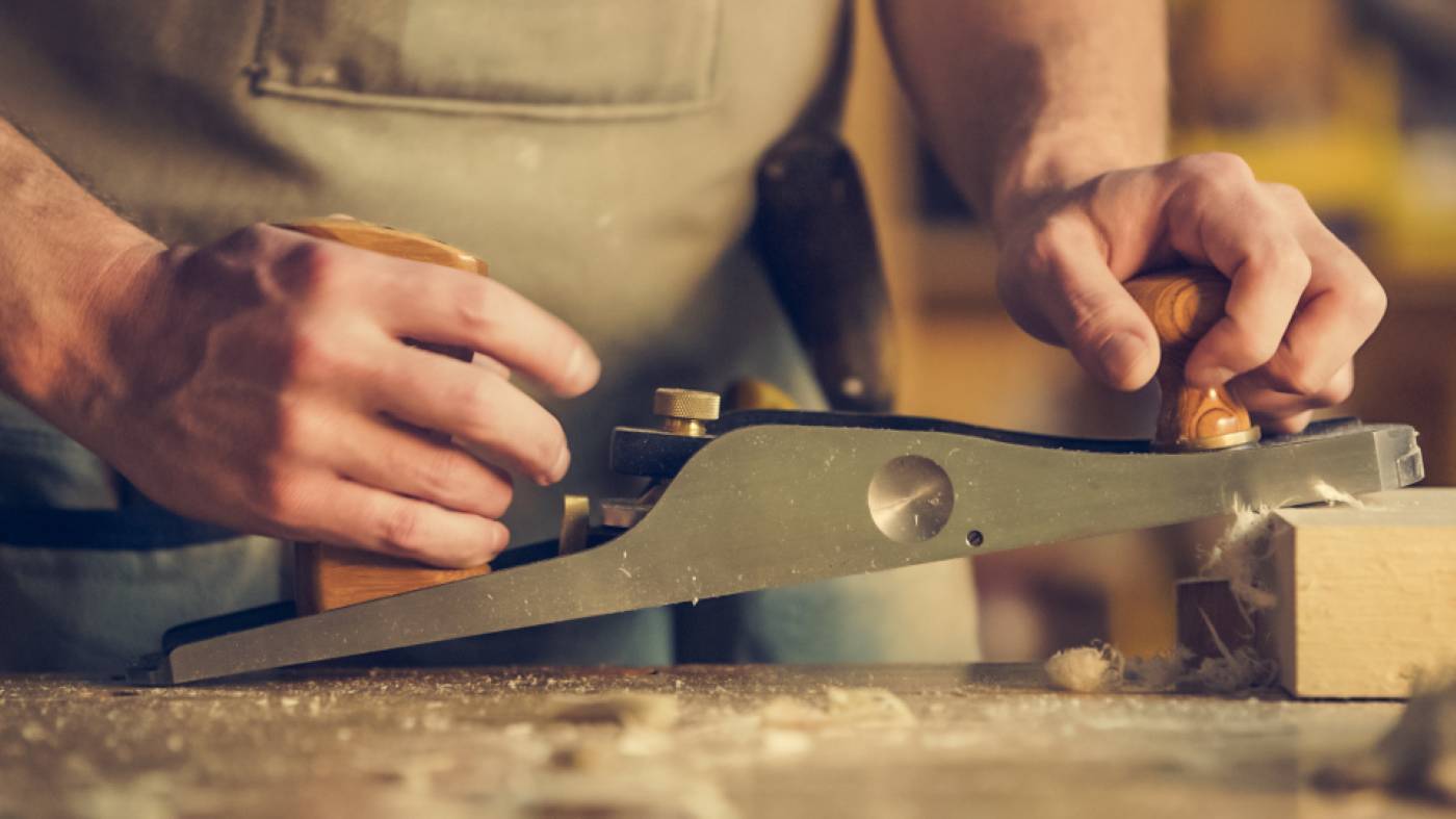 Manos de un maestro trabajando madera con un cepillo de carpintero.