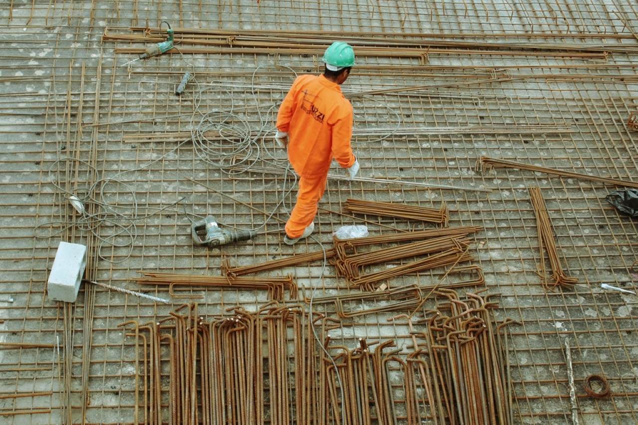 Trabajador con casco y overol naranja caminando sobre la enfierradura de una losa en construcción.