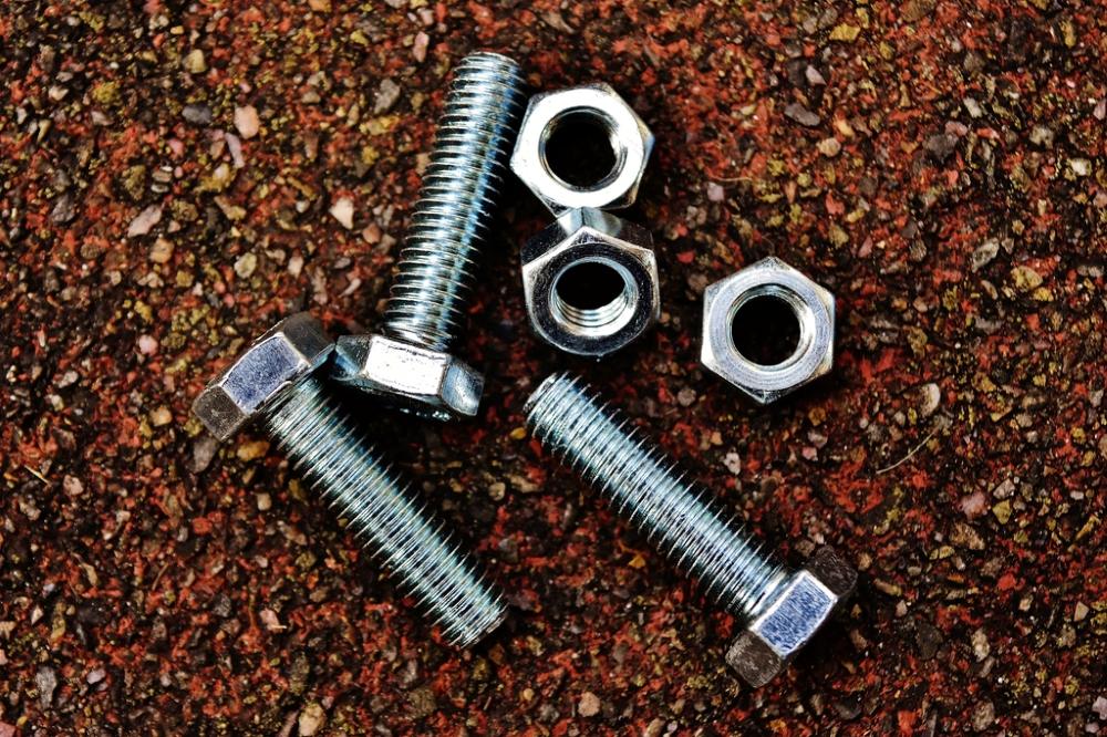 Pernos hexagonales zincados y tuercas sobre una superficie de metal oxidado.