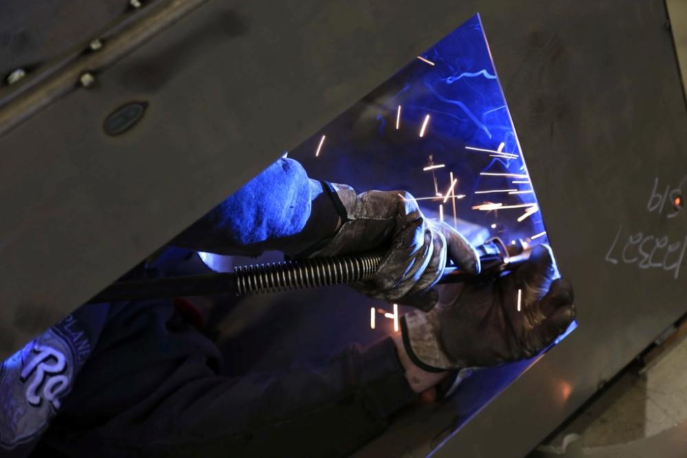 Soldador con guantes de cuero trabajando una plancha de acero entre chispas.